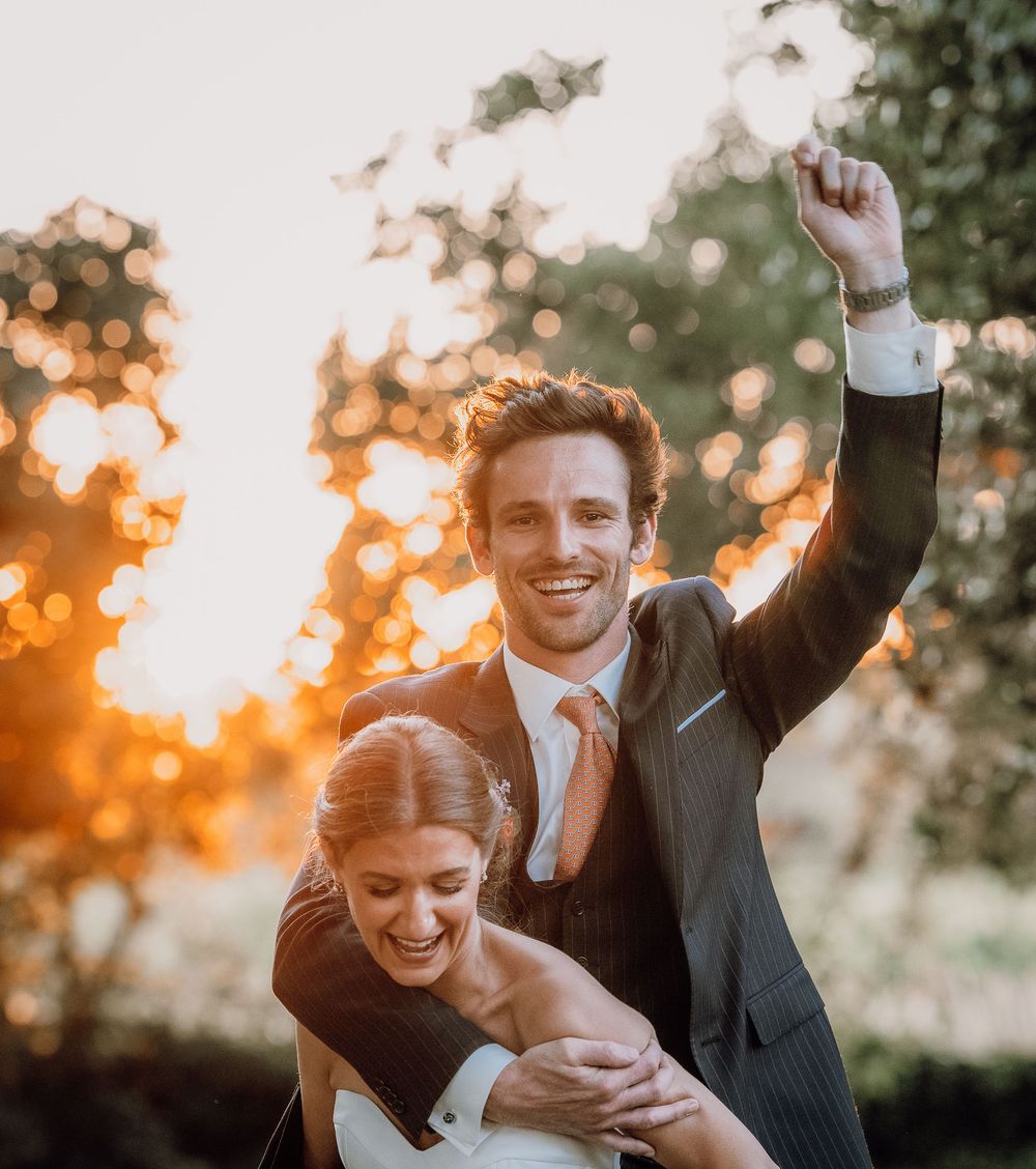 Happy wedding couple embraces and celebrates during golden sunset with warmly lit bokeh backdrop.