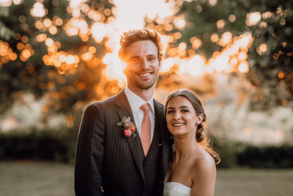 Wedding couple poses at sunset in a natural outdoor setting with golden sunlight filtering through trees behind them.