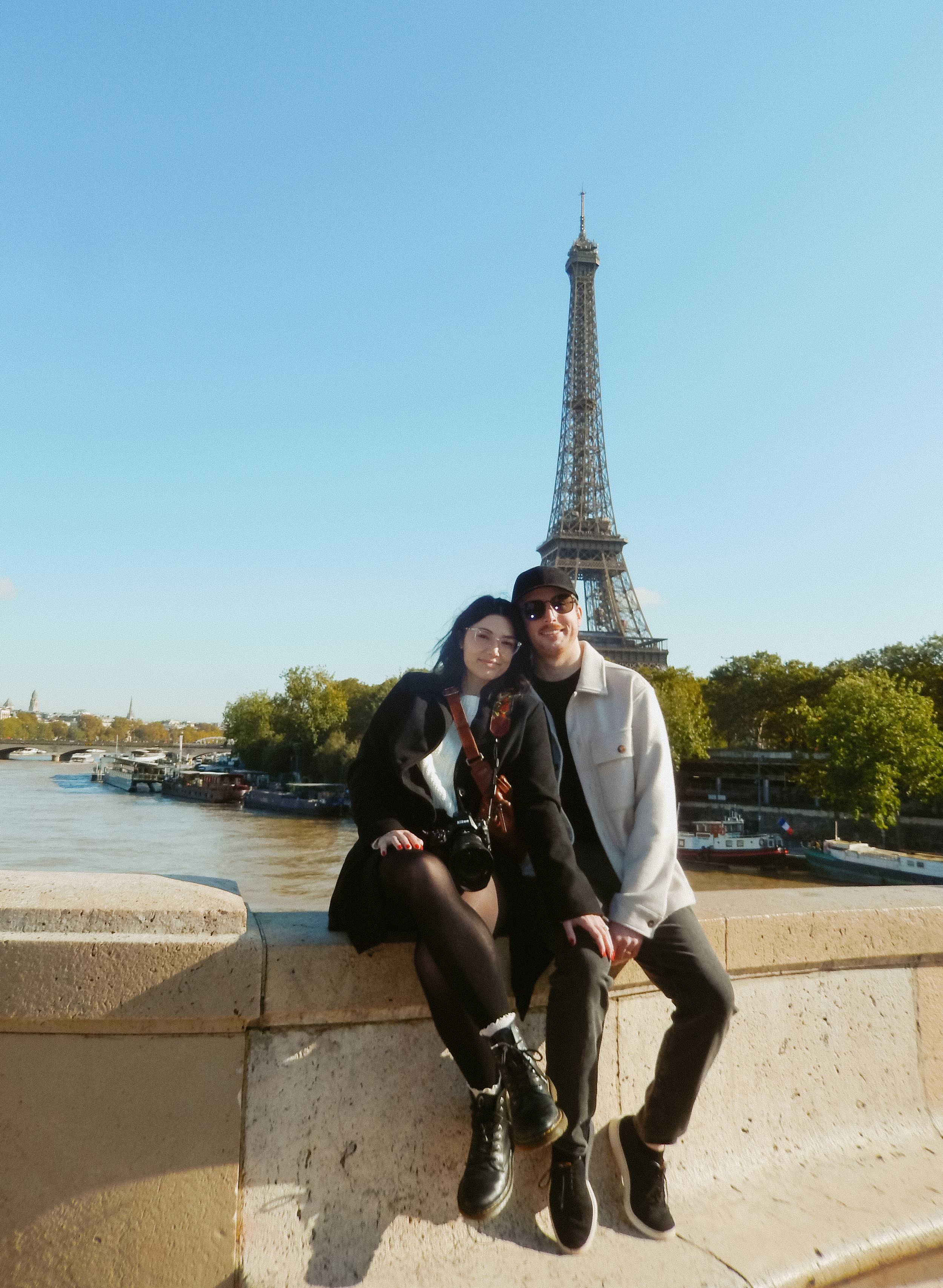 Tourists taking photos with Eiffel Tower in background on sunny Paris day.