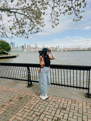 A sequence of photos showing a person taking pictures of the Manhattan skyline from a waterfront promenade.