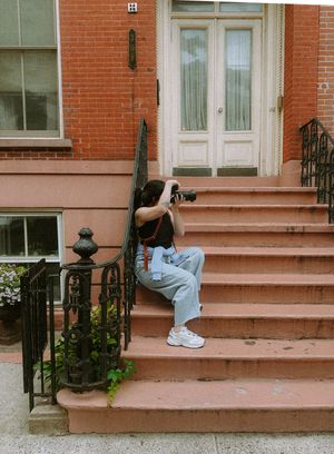 A person sits on pink painted brownstone steps with black iron railings in an urban setting.