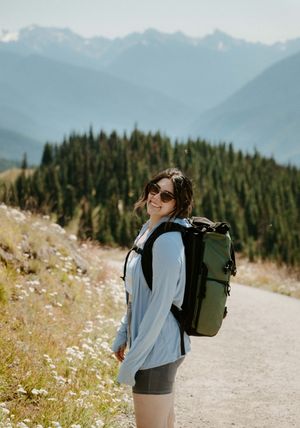 Hiker enjoying mountain views on trail surrounded by wildflowers.