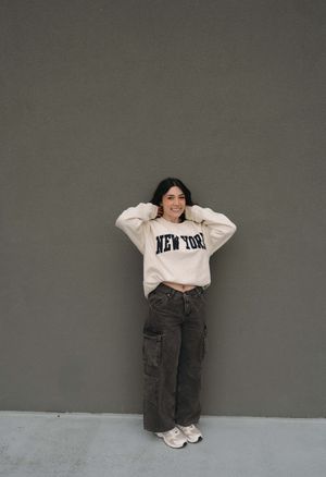 A person in a white sweatshirt and grey cargo pants poses against a grey wall in four different casual positions.