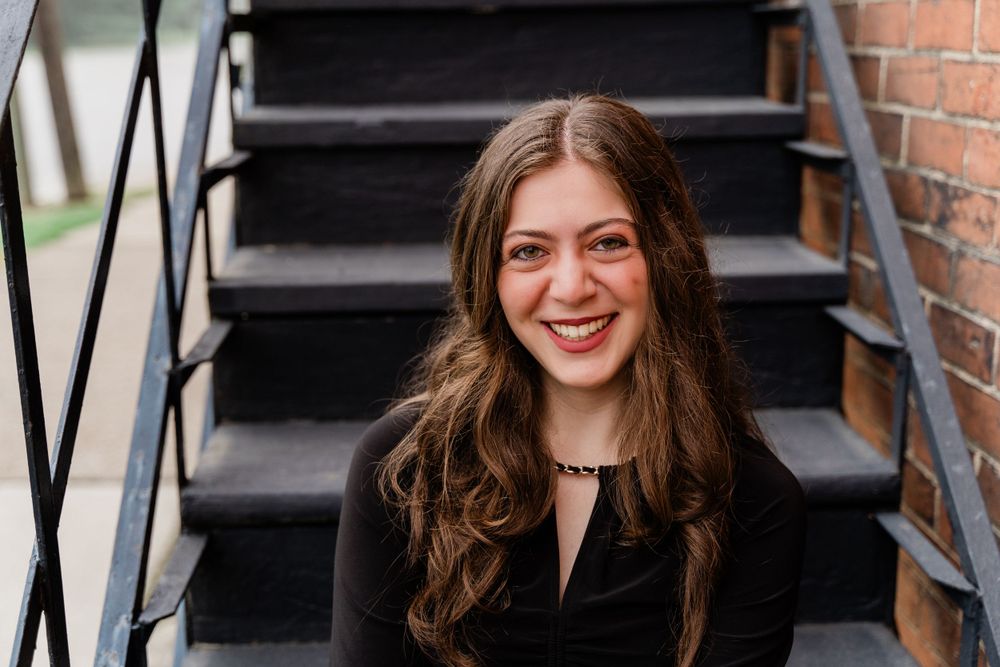 Portrait shot on black metal stairs showing casual fashion with black top and flowing hair.