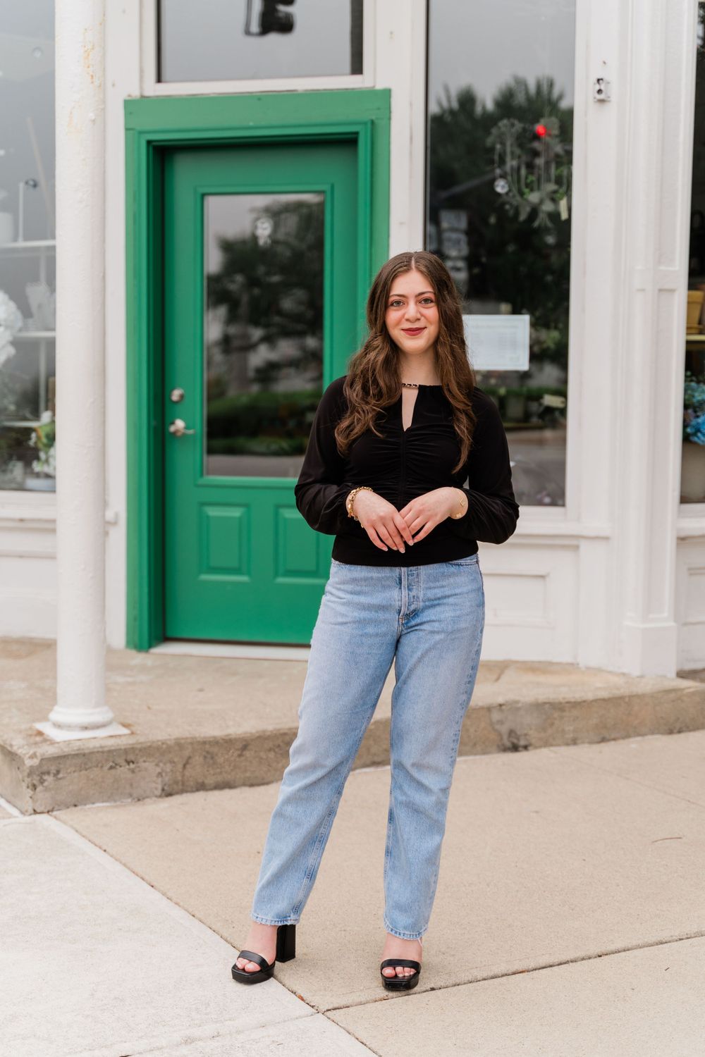 A stylish outfit featuring light wash jeans and a black top paired with sandals in front of a bright green door.