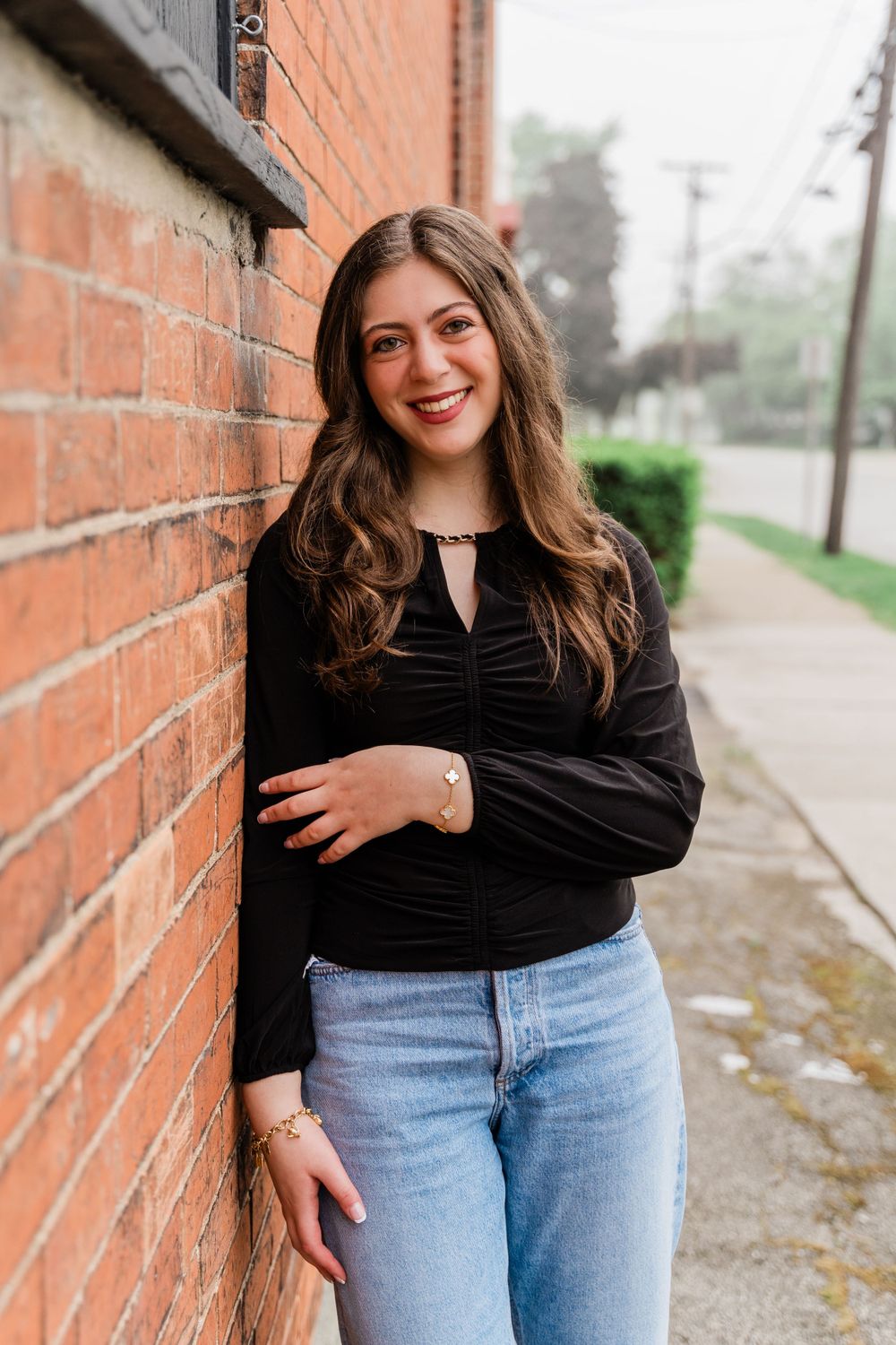 Street style portrait against red brick wall wearing classic black top and light wash denim.