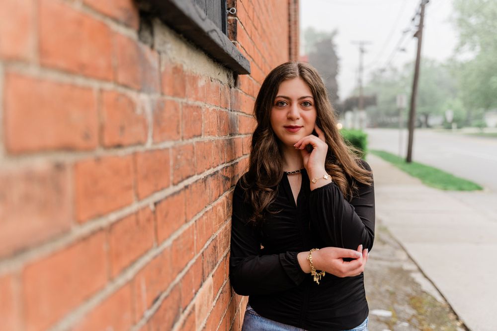 Thoughtful pose against brick wall wearing casual black top and light denim jeans.