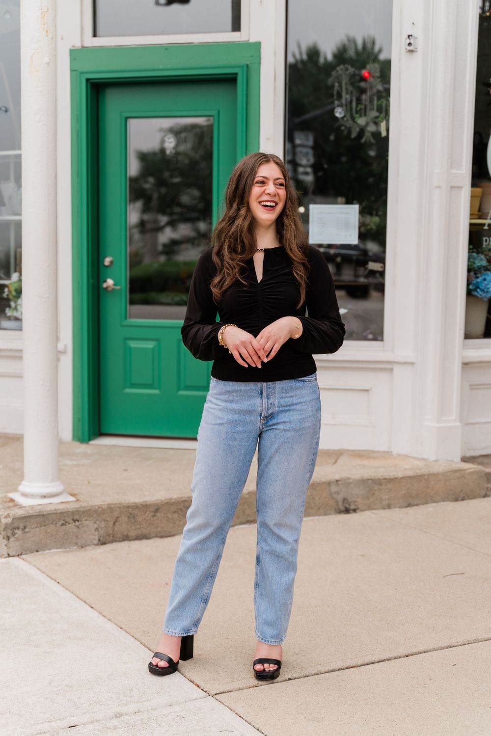Casual street style look with a black long sleeve top and light denim in front of a green storefront door.