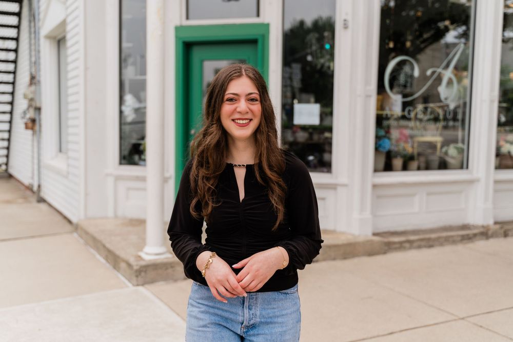 Casual spring fashion with a black keyhole top and light wash jeans against a white storefront.