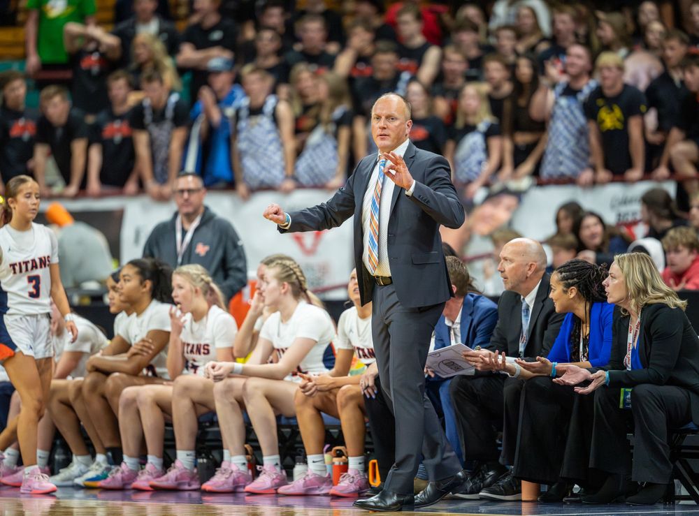 Coach gestures from sideline while team sits on bench during basketball game.