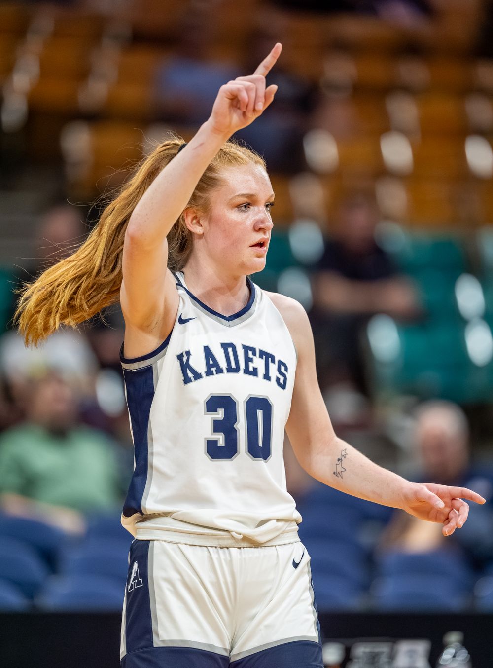 Basketball player points upward while directing teammates during game.