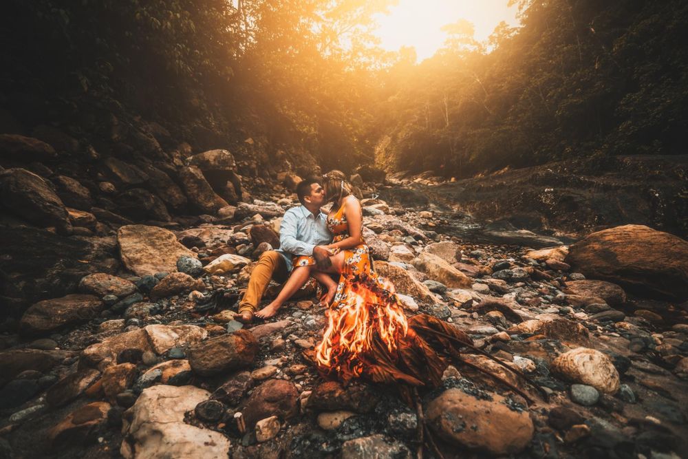 A cozy campfire scene with two people enjoying the warm glow among rocky terrain at sunset.