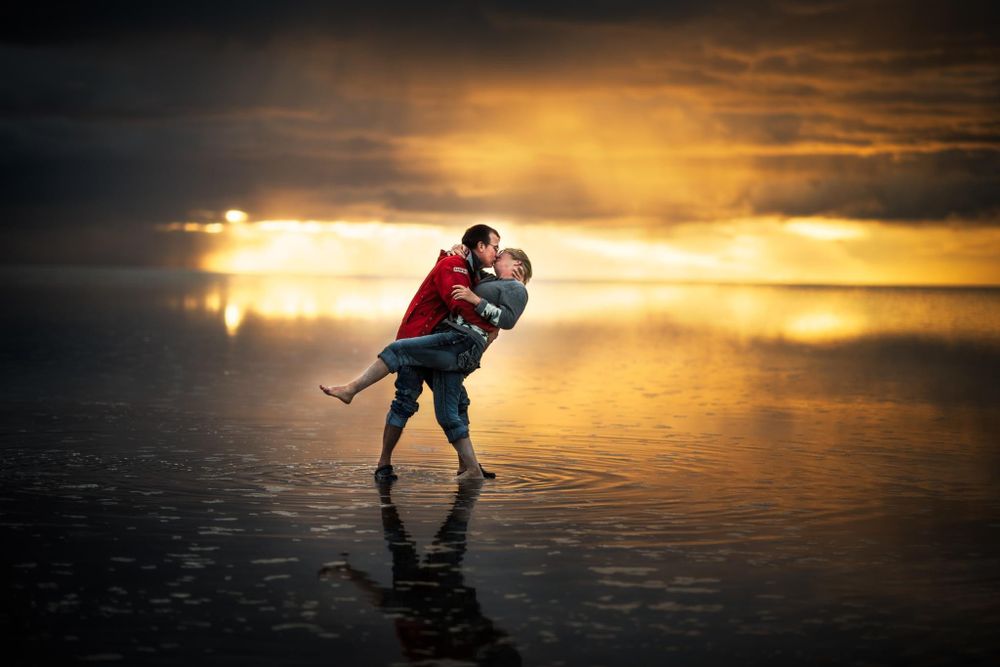 A romantic silhouette embraces against a golden sunset reflecting on still water.