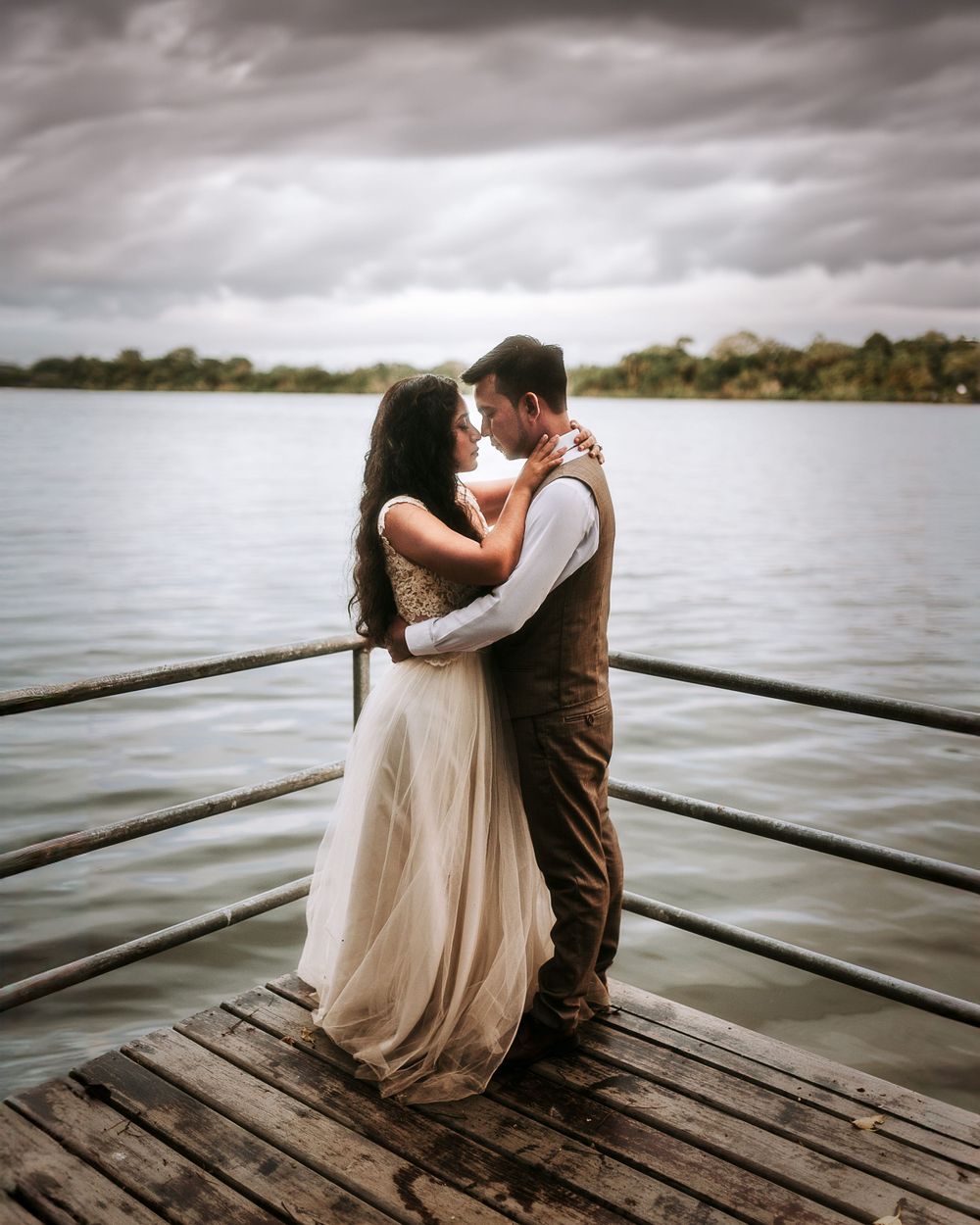 Romantic couple embracing on wooden dock overlooking serene lake at sunset.