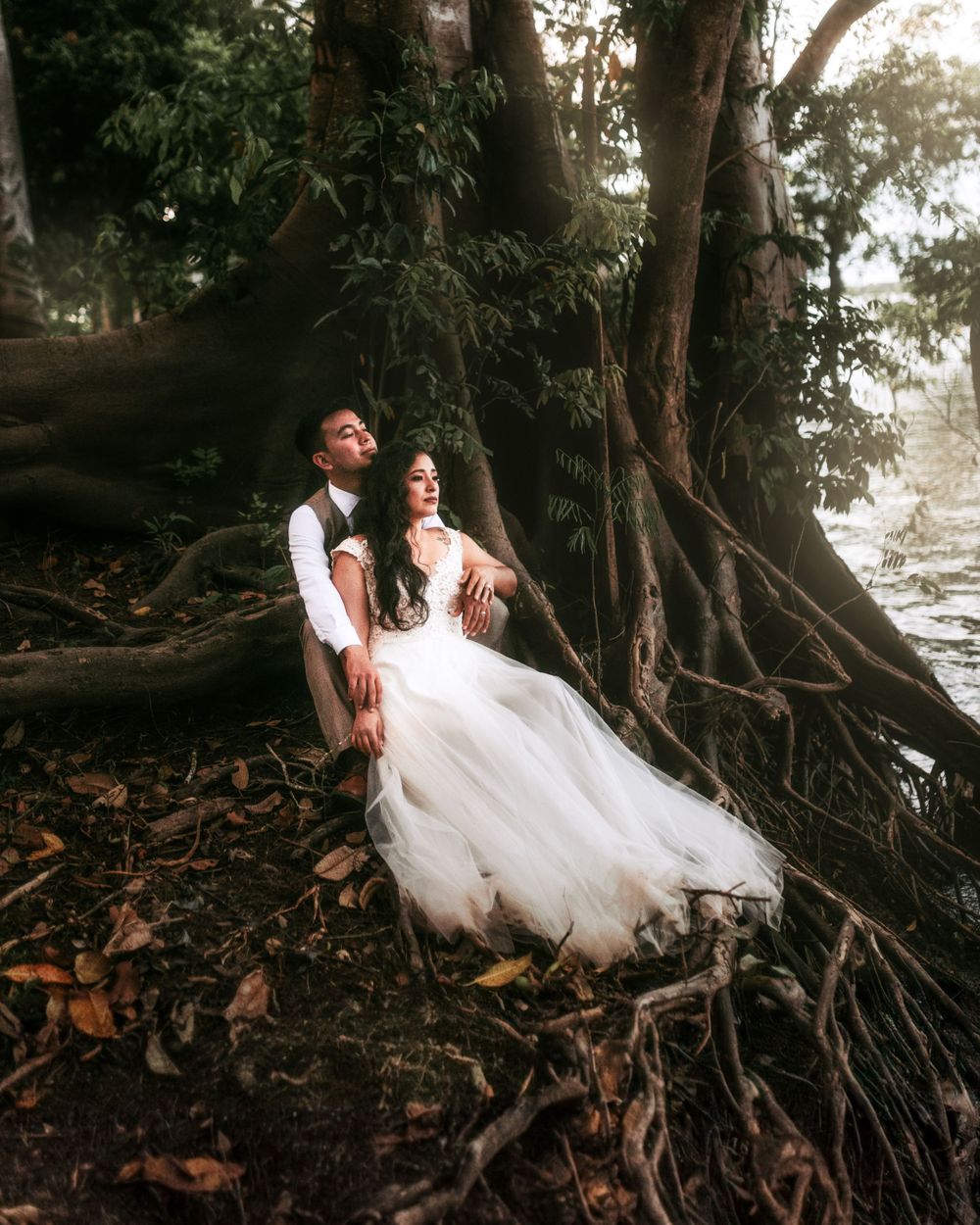 Wedding couple sitting among exposed tree roots in a mystical forest setting.