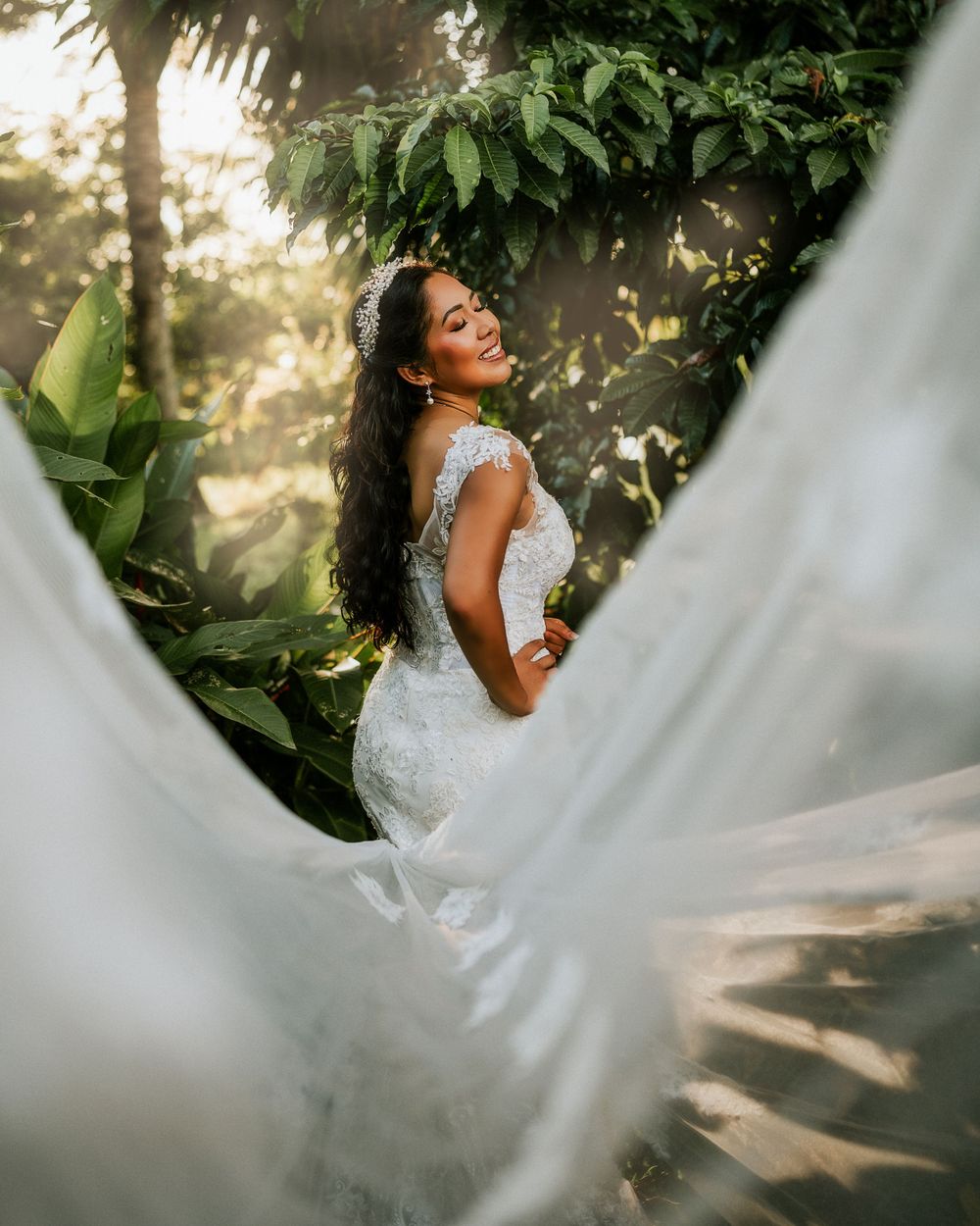 Beautiful wedding dress flowing in sunlit tropical garden with lush greenery and golden hour lighting.