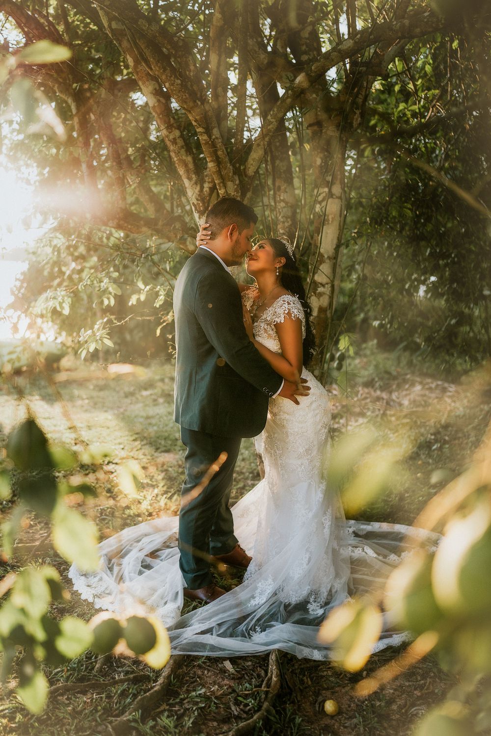 Romantic wedding photo captured in dreamy sunlit forest with flowing white dress and trees creating magical atmosphere.