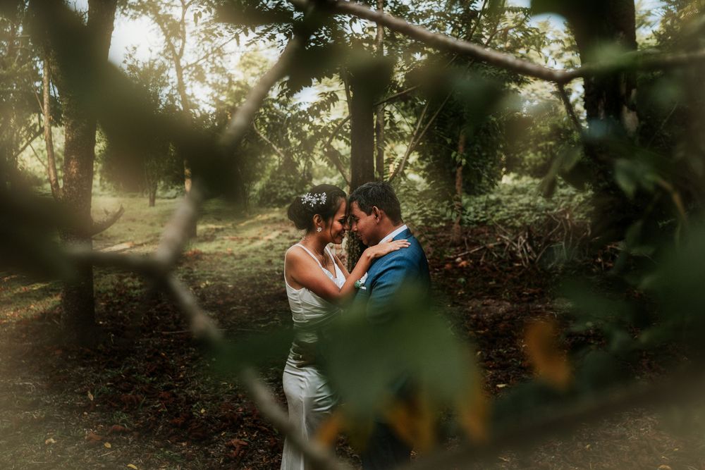 Two people share a romantic moment in a sunlit garden setting framed by natural foliage.