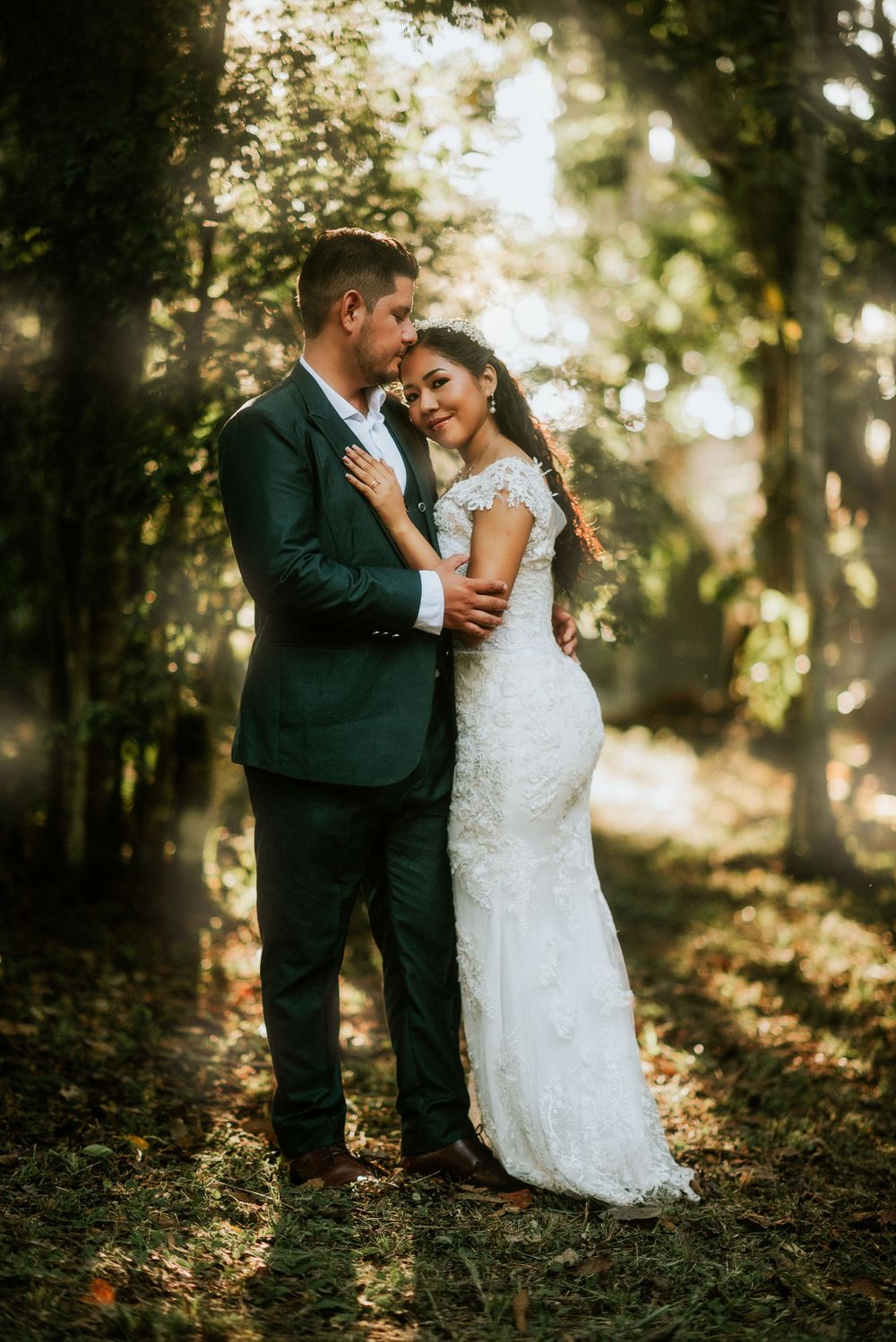 A romantic wedding photo of a couple embracing in a sunlit forest setting with dreamy golden hour lighting.