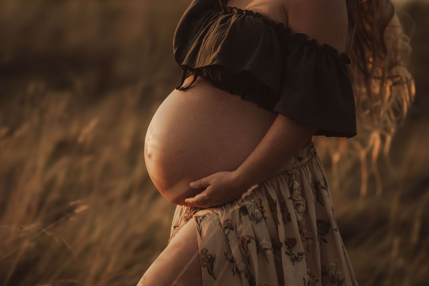 Close-up silhouette of a pregnant belly against a sunset sky.