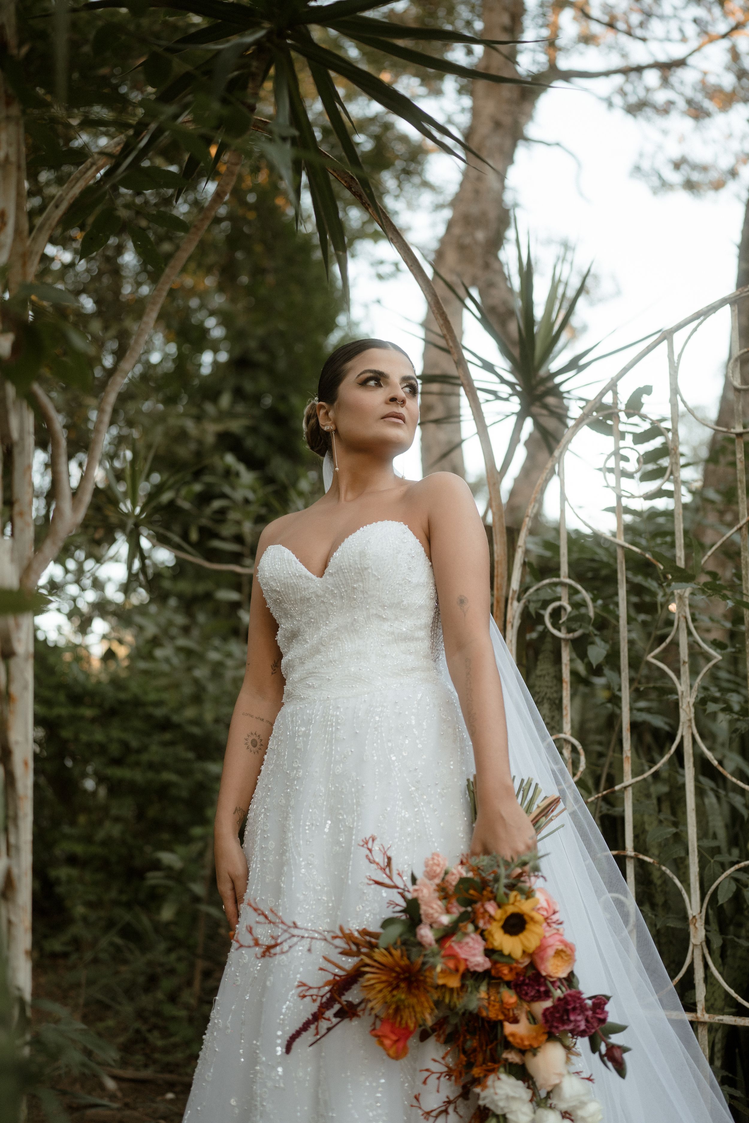 Bridal portrait with autumn-themed bouquet against iron gate backdrop in forest setting.