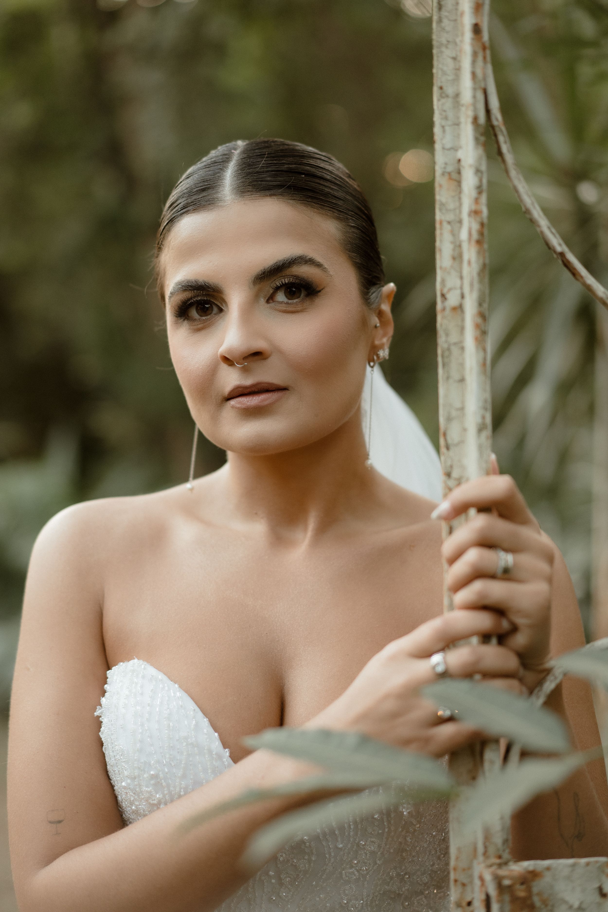 A bride in a strapless white wedding dress poses outdoors in a natural setting.