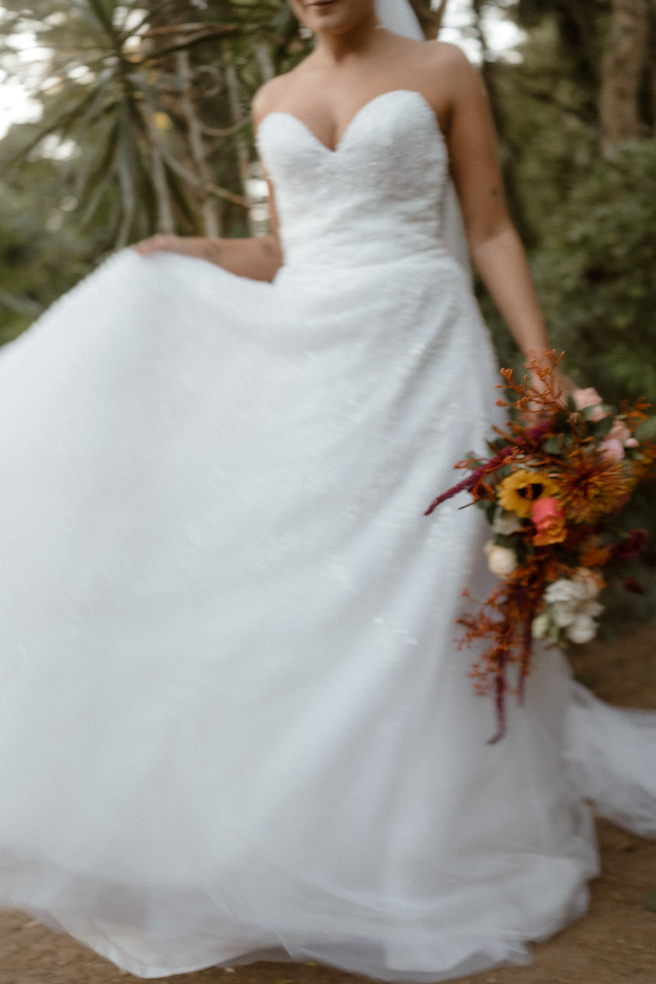 A strapless ball gown wedding dress with a vibrant autumn bouquet in a garden setting.