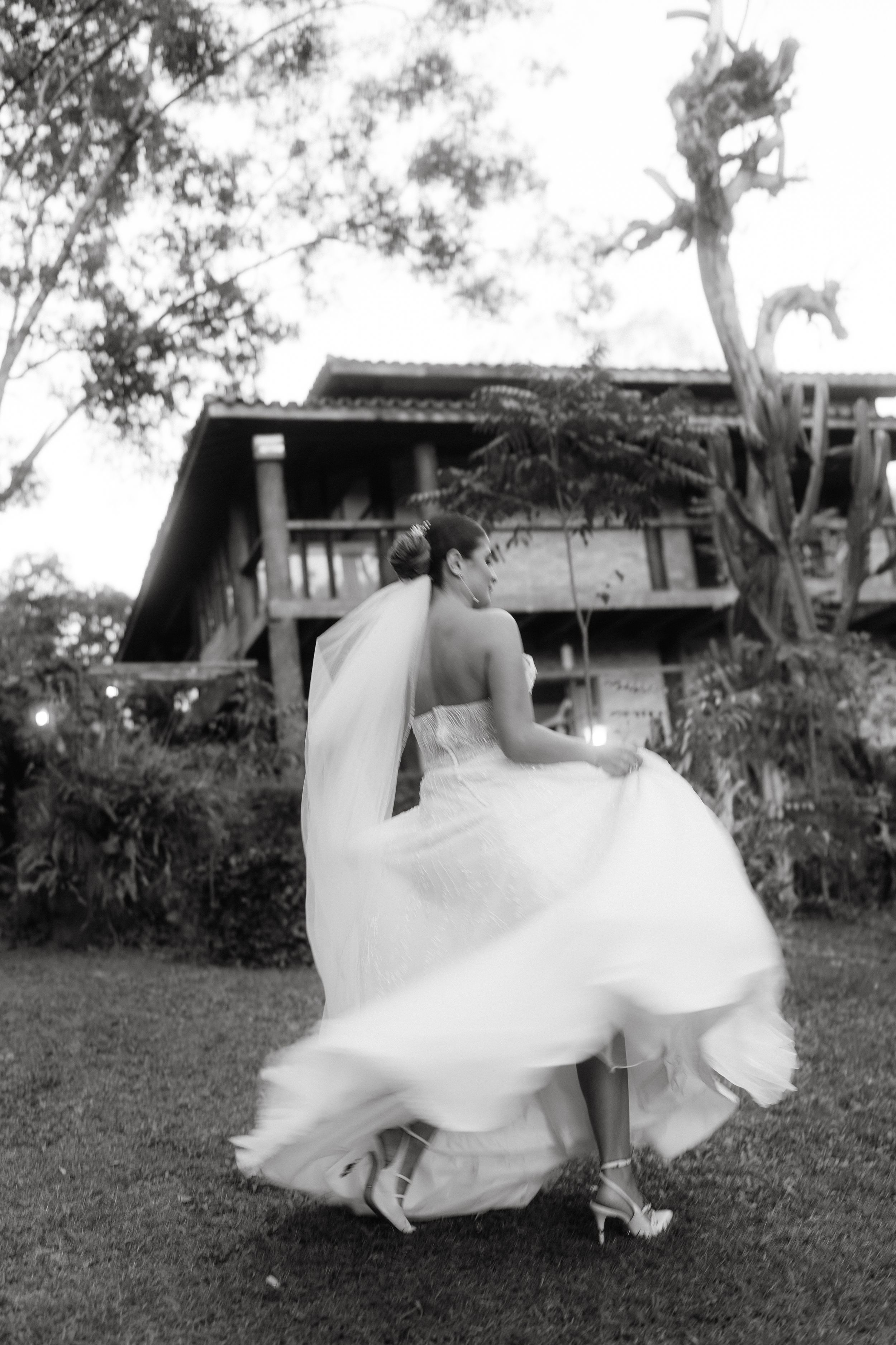 A flowing white wedding dress twirls gracefully against a rustic house backdrop in black and white.