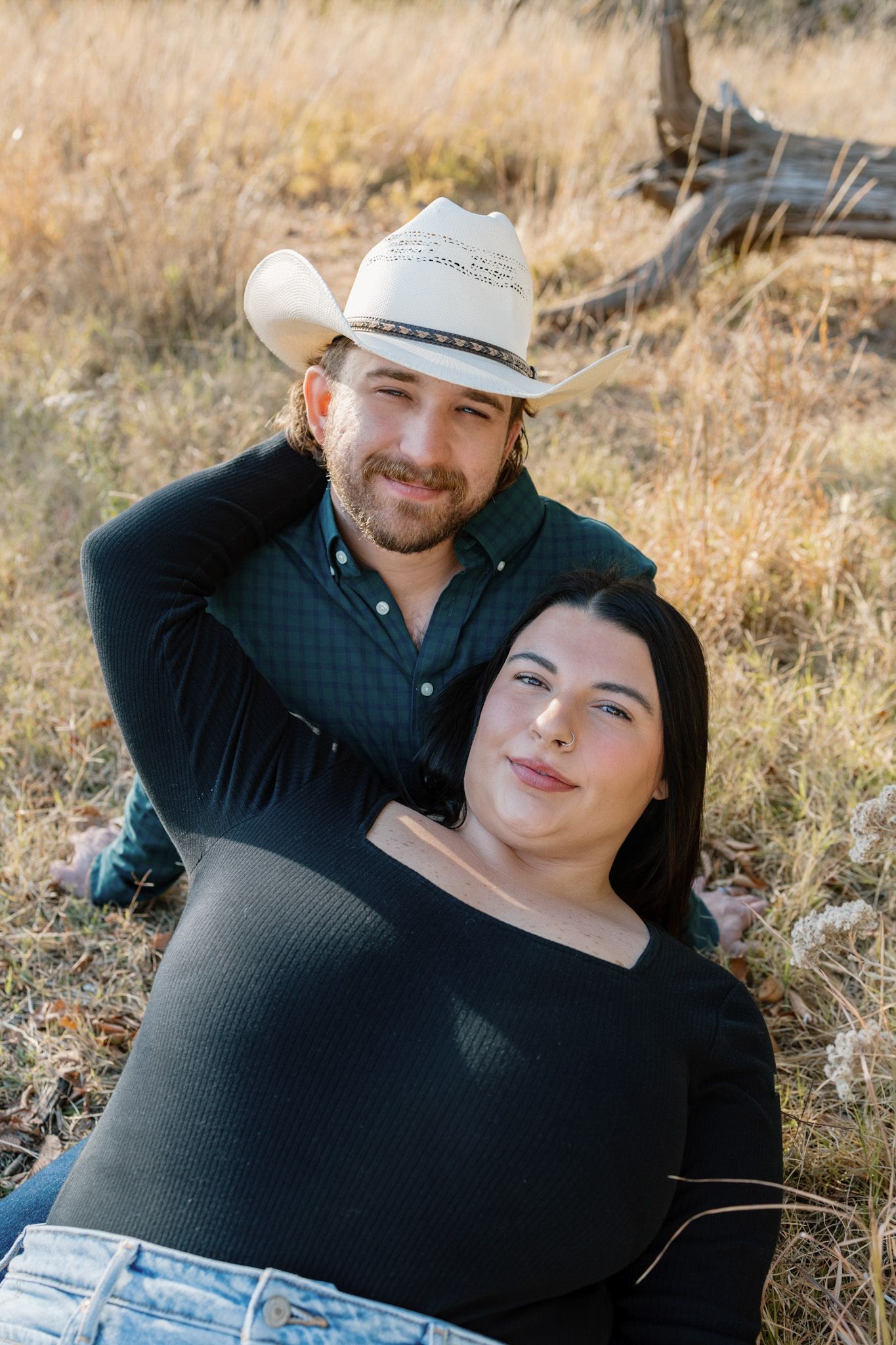 Couple in casual western wear pose together in autumn field.