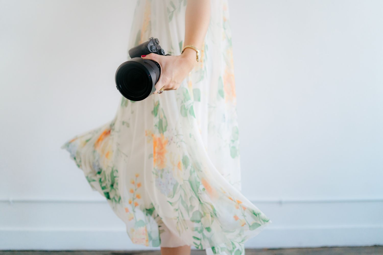 A flowing floral dress caught in motion against a white background with a camera in hand.