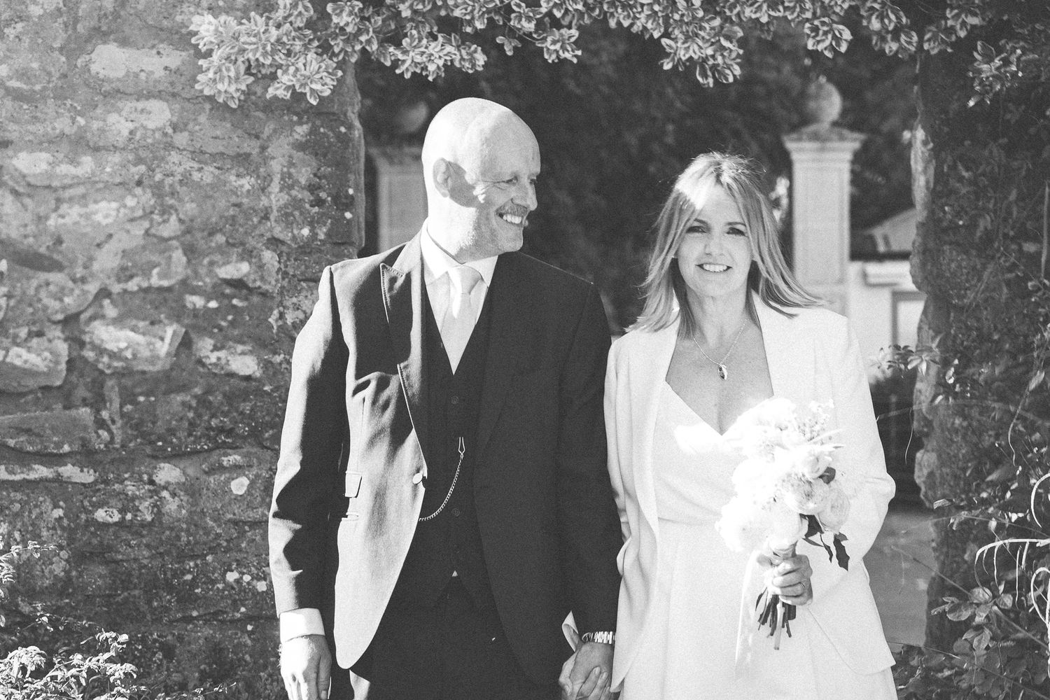 Black and white wedding portrait outdoors against stone wall backdrop.