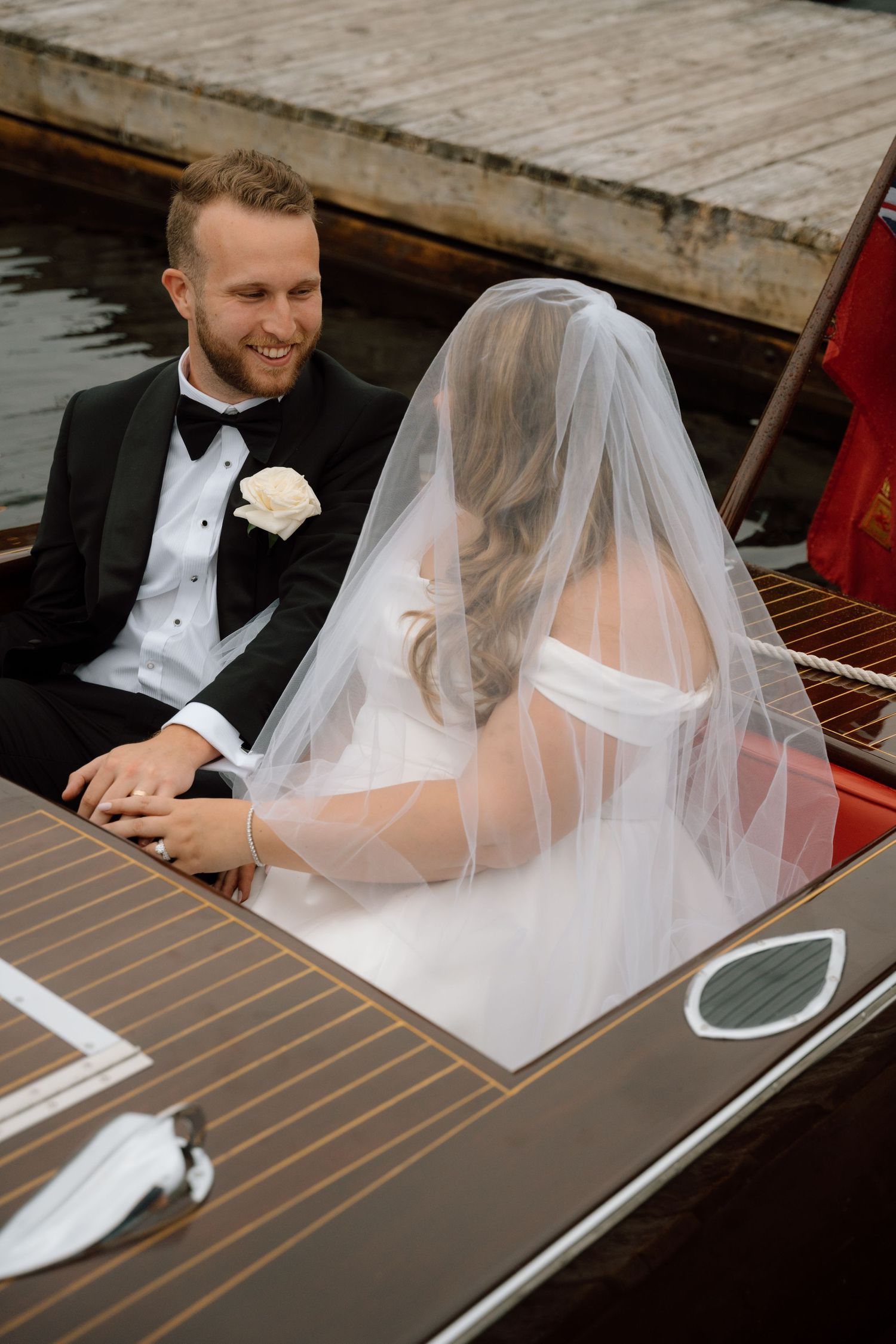 A couple in formal attire sit together in an elegant wooden boat.