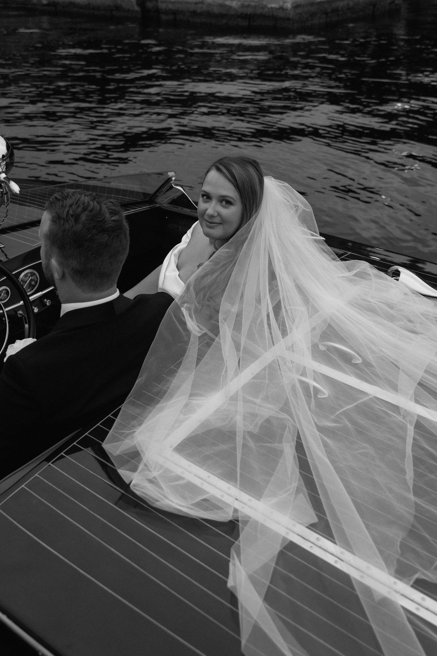 A flowing white veil billows in the wind on a classic wooden boat.