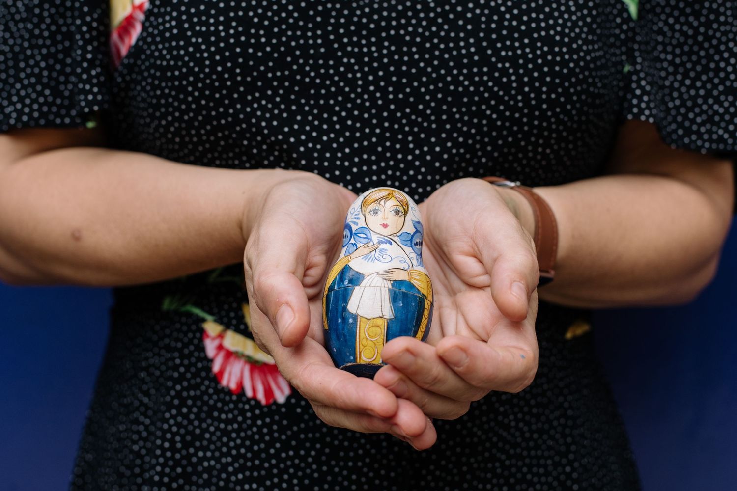 Hands holding vintage black and white portrait photographs against a dark blue background with yellow floral pattern.