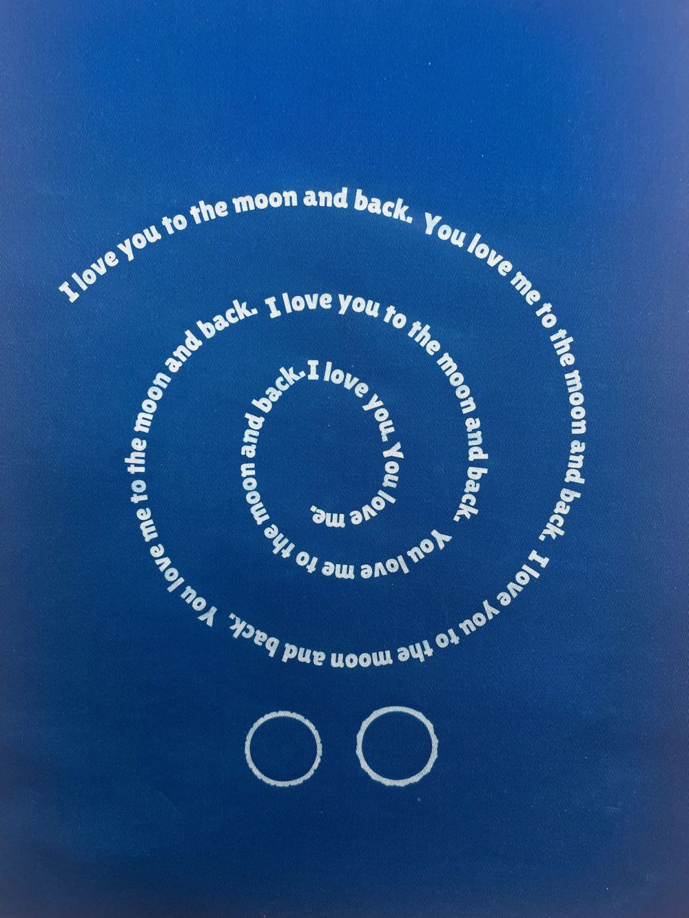 White text spirals in a circular pattern against a deep blue background saying 'I love you to the moon and back' repeatedly.