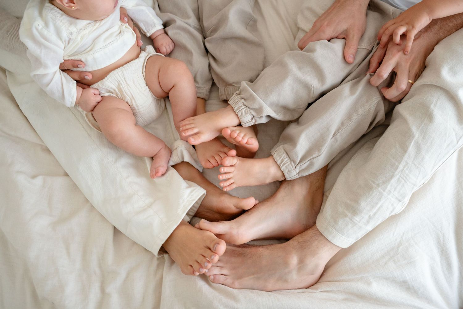 A series of tender moments showing hands gently holding and caressing a baby's tiny feet on white fabric.