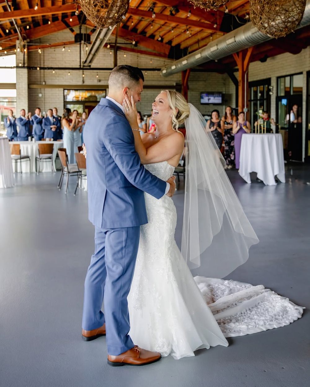 Couple sharing their first dance in rustic wooden venue with exposed beams and natural lighting.
