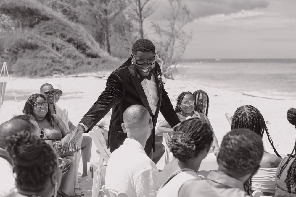 Black and white photo showing a group of wedding guests dancing and celebrating at an outdoor reception.