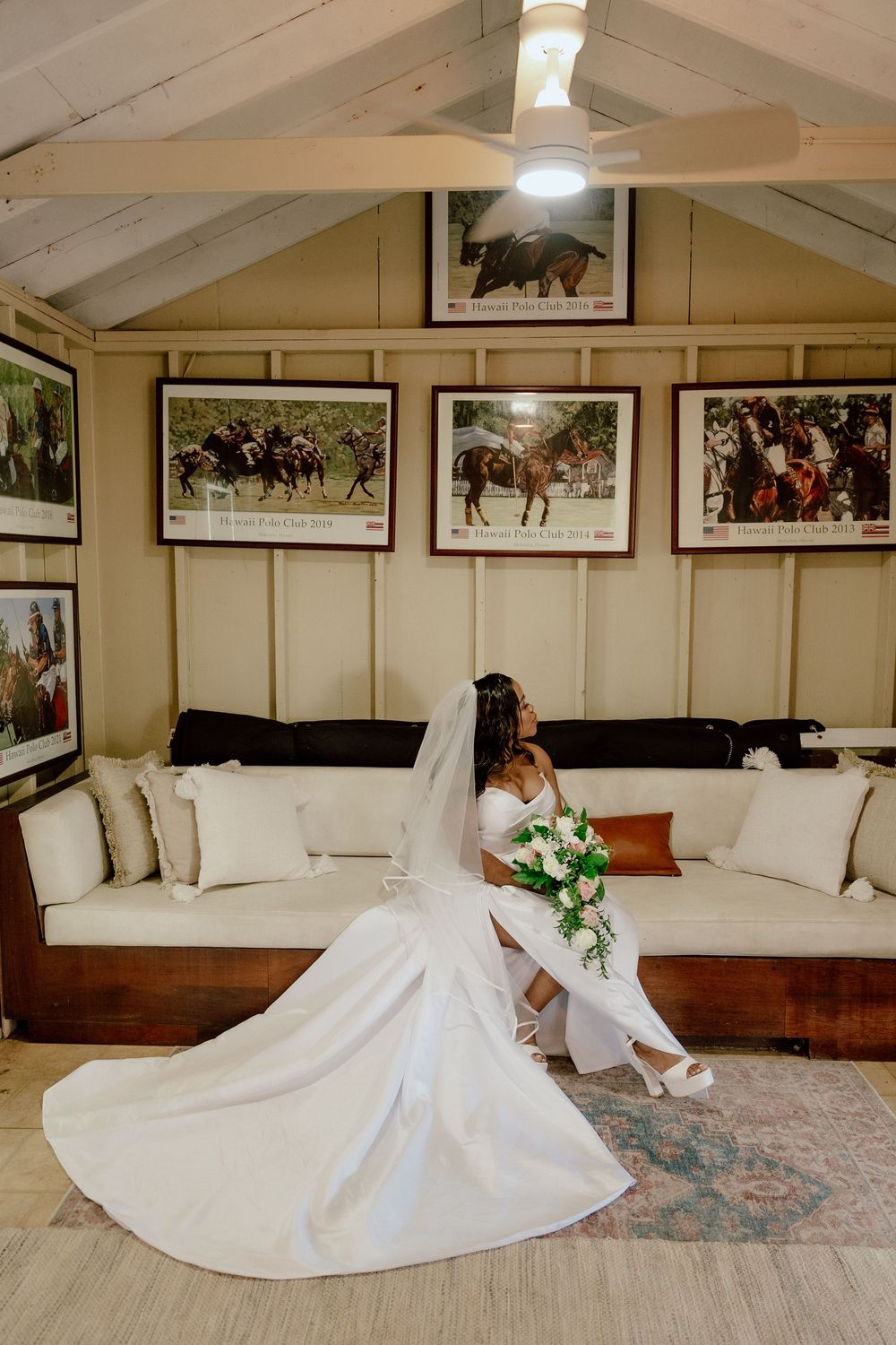 White wedding dress flowing elegantly across a carpeted room with framed photos on the walls.