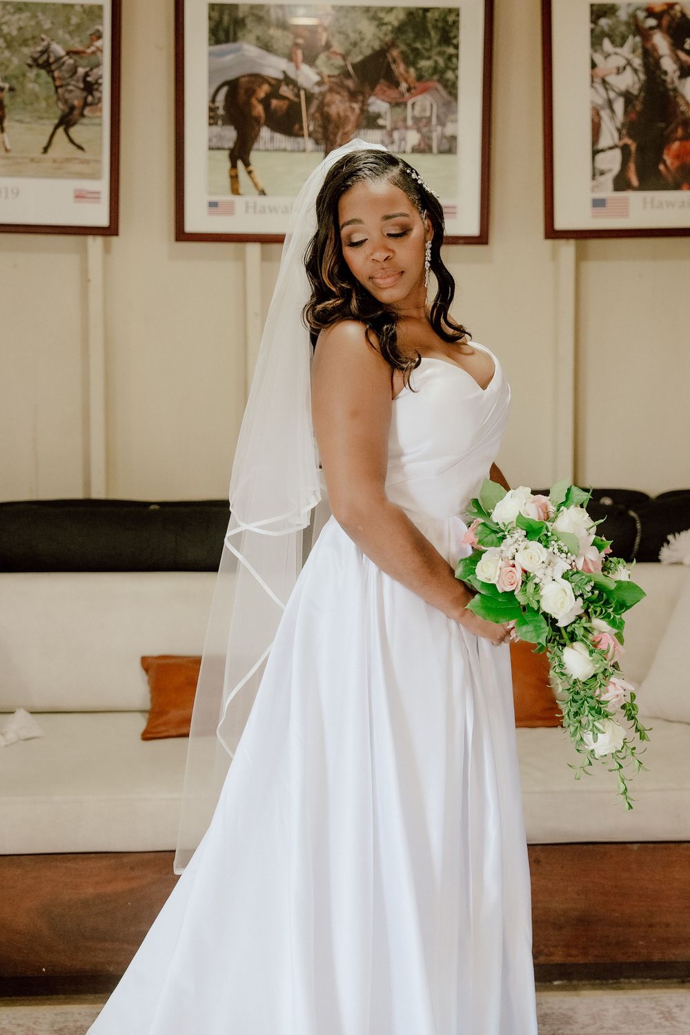 Elegant white wedding gown with cascading fabric displayed in an indoor venue with decorative wall art.