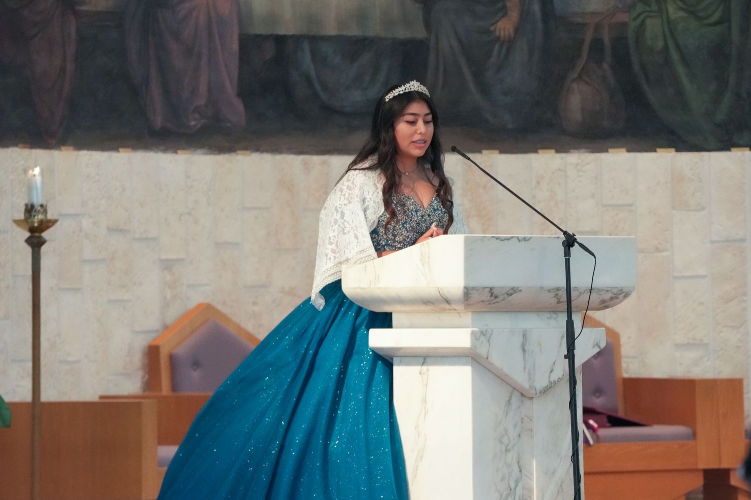A performer in a vibrant blue ball gown sings at a microphone in a church setting.