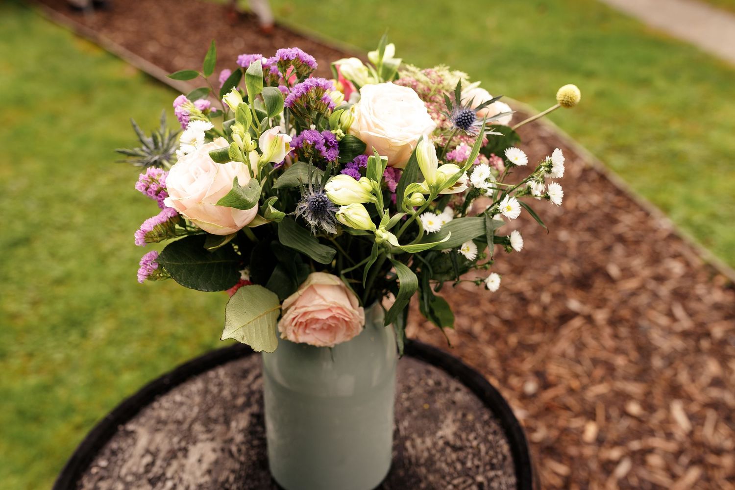 A series of potted flower arrangements with roses and mixed blooms displayed on a garden path with mulch border.