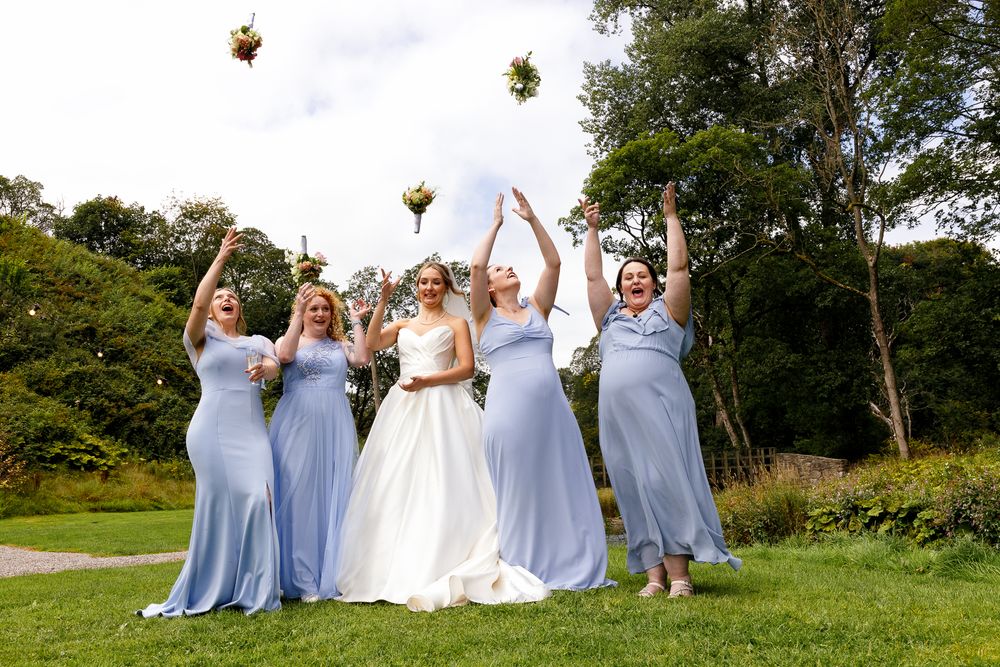 Wedding party in light blue bridesmaid dresses poses joyfully on a grassy hill during an outdoor celebration.