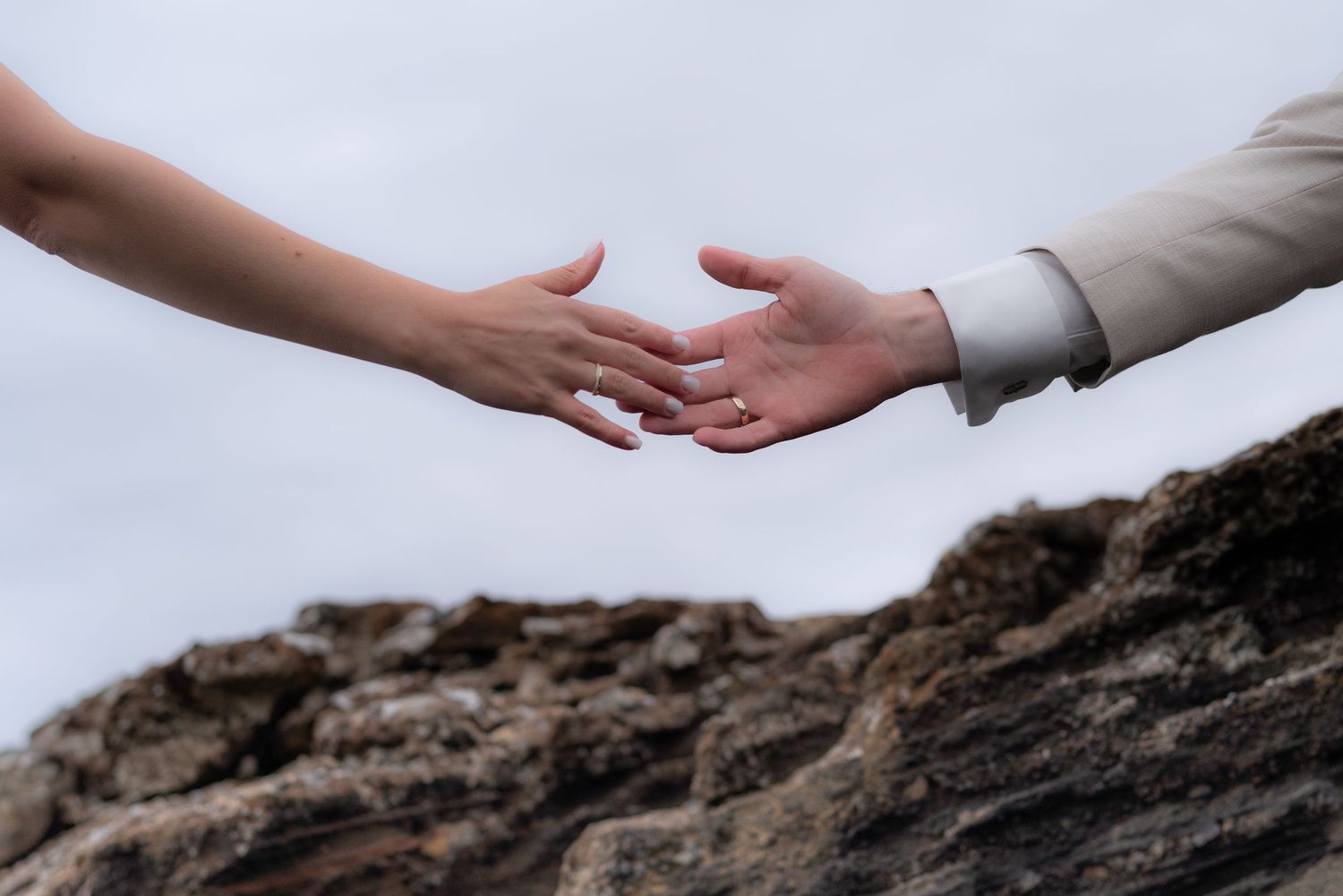Two hands reach across a rocky cliff edge against a blurred natural background.