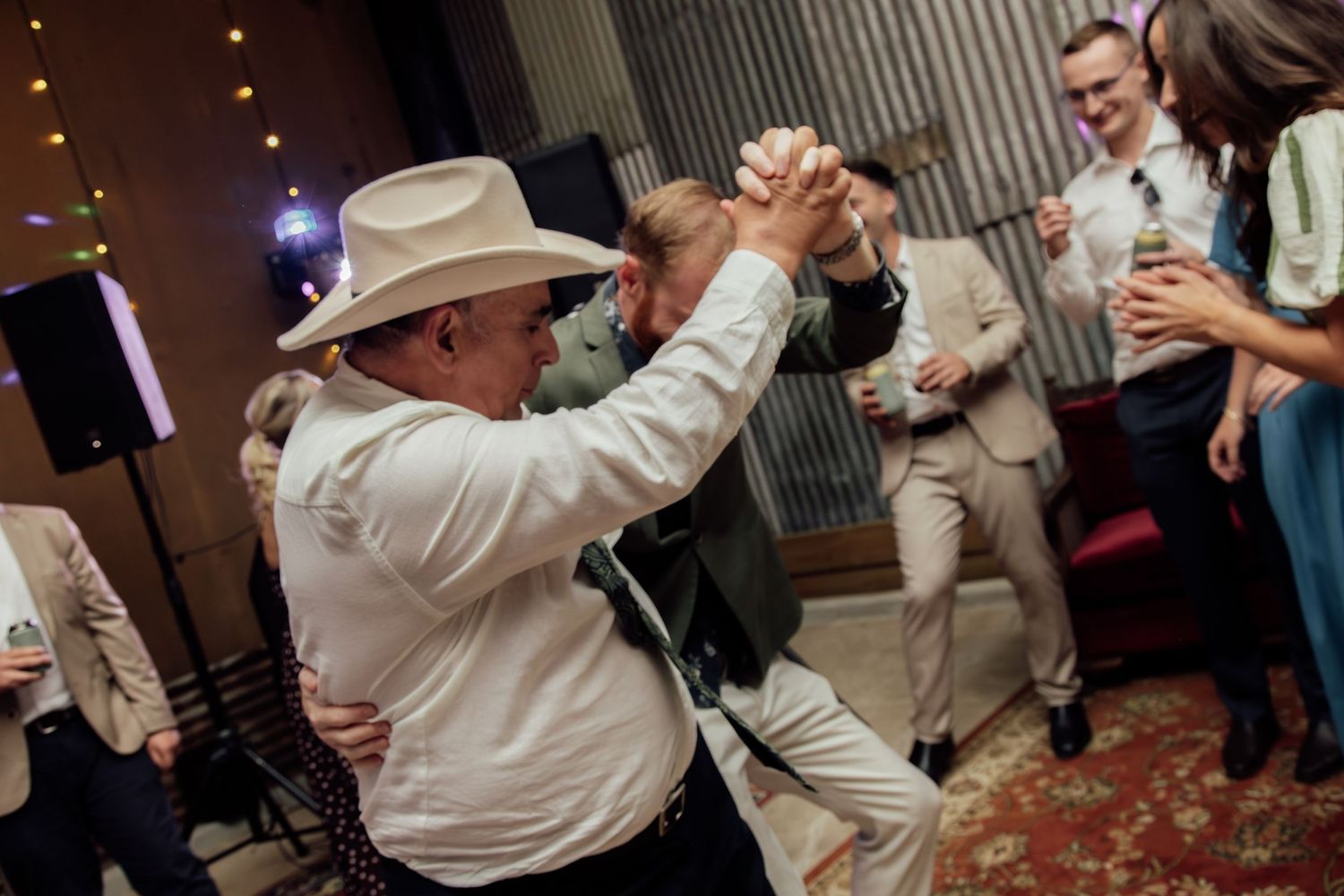 Wedding guests dancing and celebrating together at a reception with warm lighting and festive atmosphere.