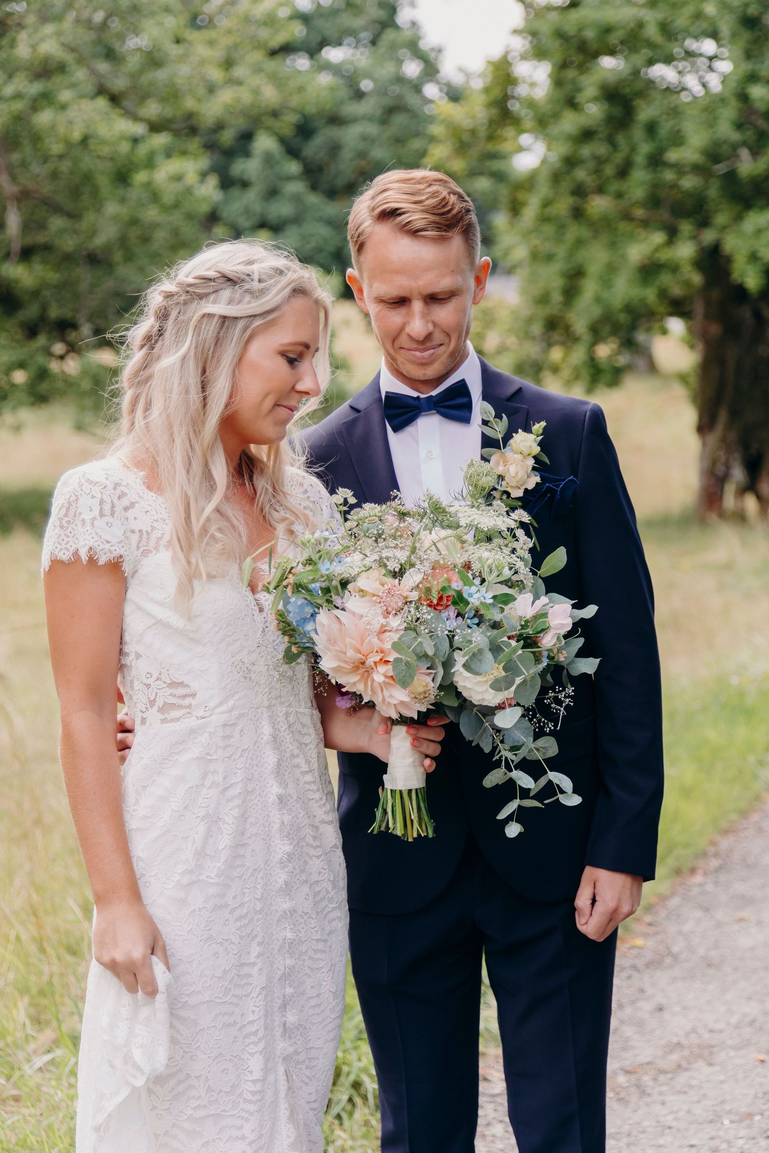 A romantic wedding couple poses outdoors with a beautiful bouquet featuring eucalyptus and pastel flowers.