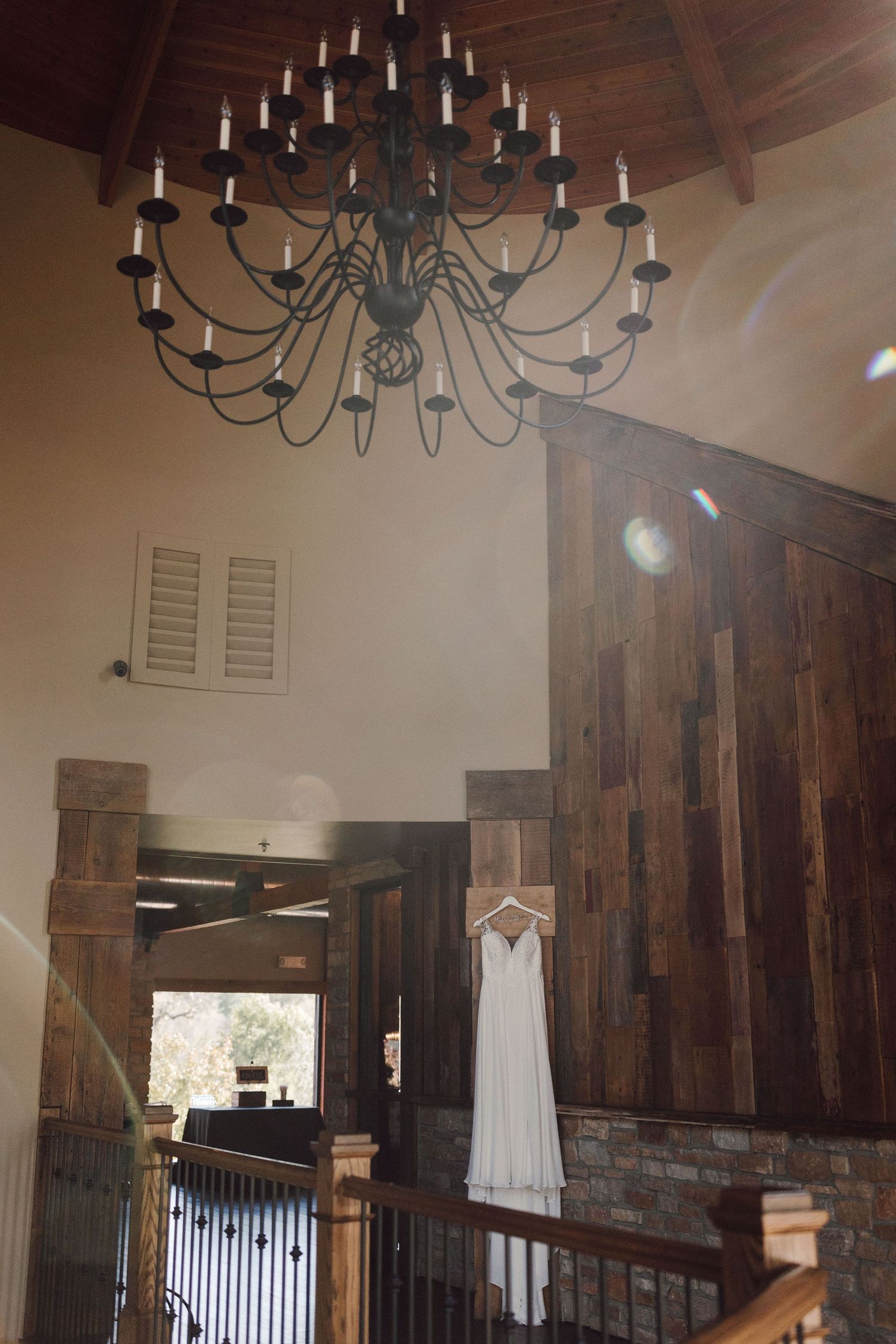 Rustic wedding venue interior with wooden walls and elegant chandelier displaying hanging dress.