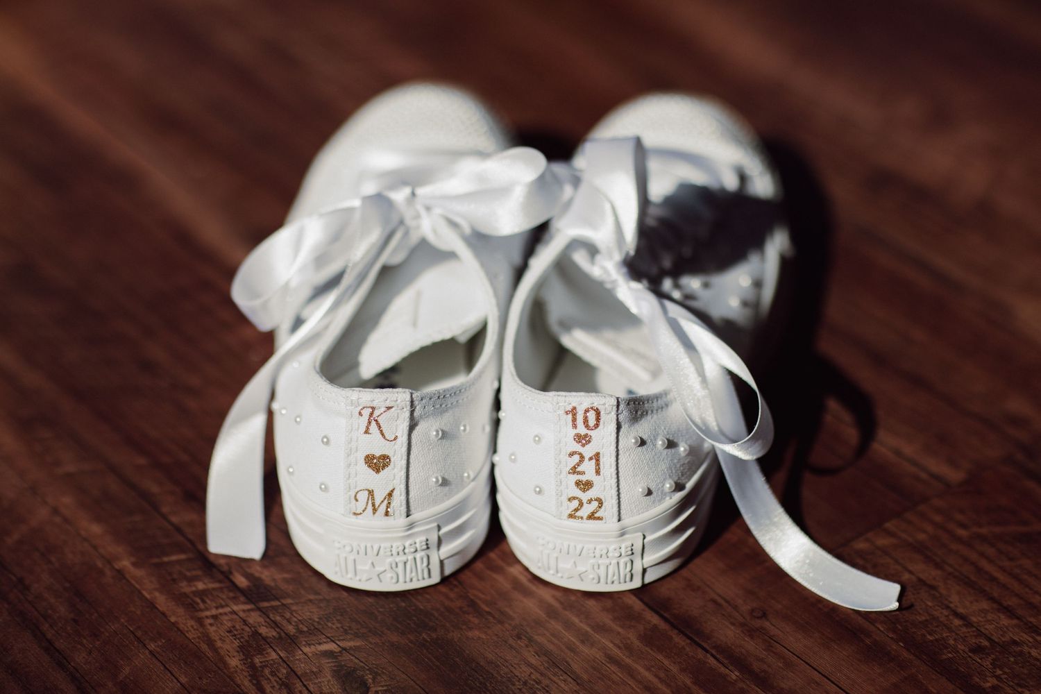 White monogrammed baby shoes arranged on dark wooden surface.