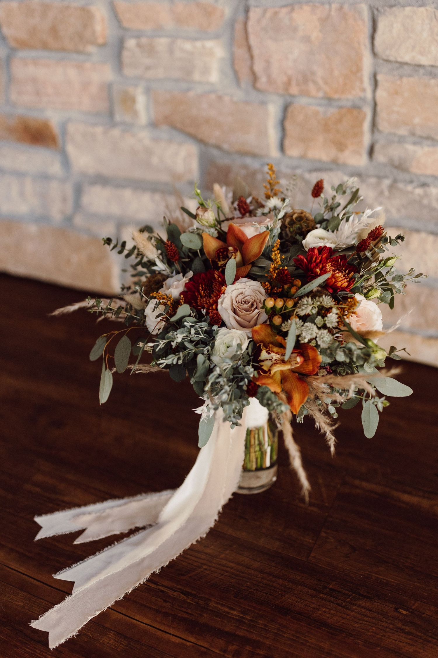 Rustic fall wedding bouquet with white ribbons featuring dried flowers and foliage against wooden surface.