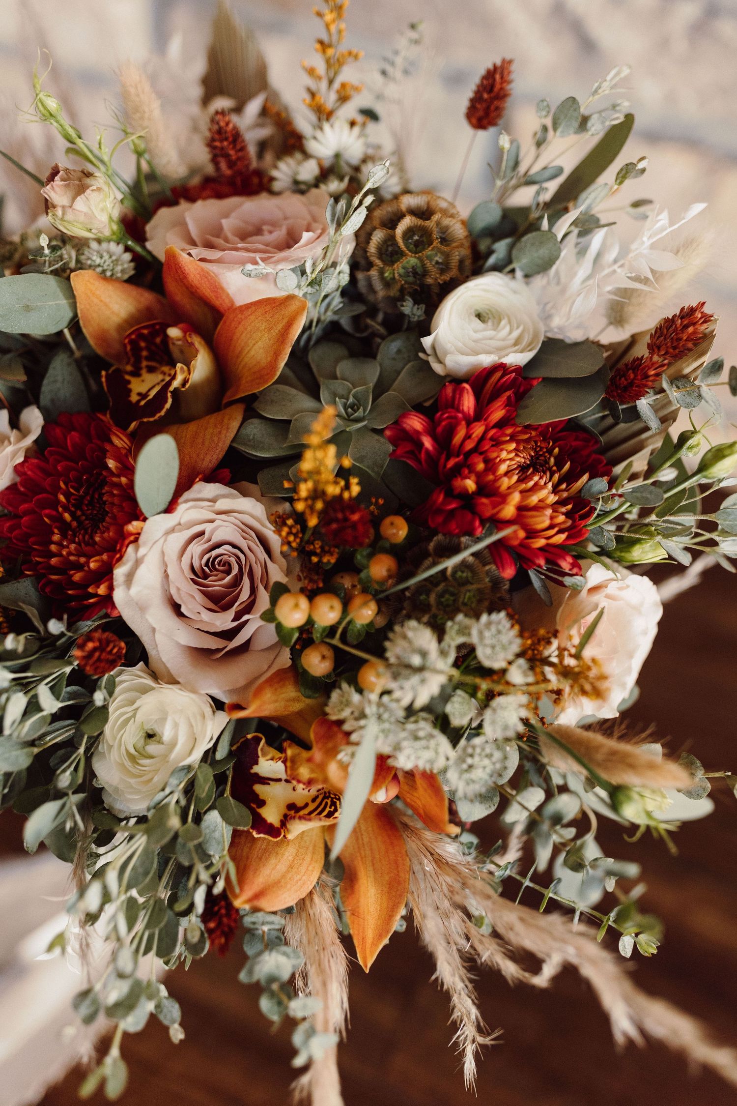 Fall-inspired wedding bouquet with roses, dahlias, and autumn foliage in warm burgundy and peach tones.